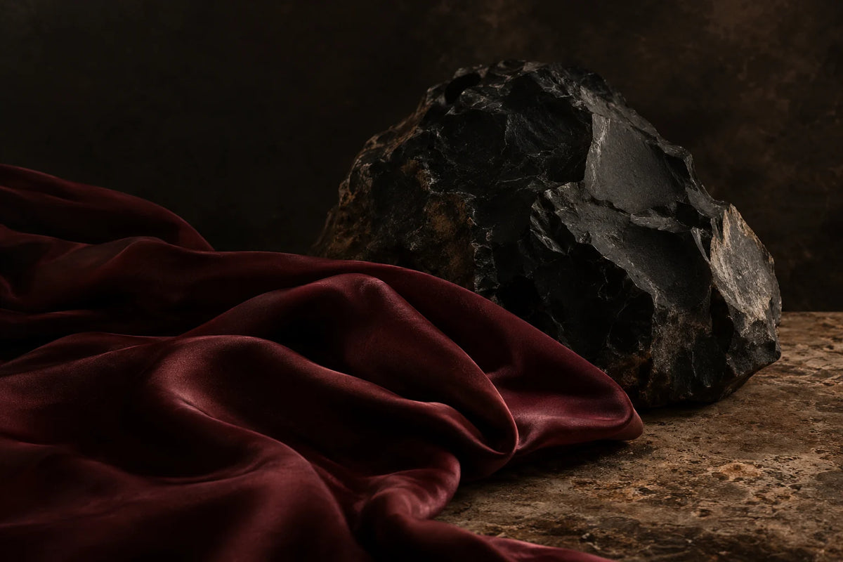 Atmospheric still life of dark stone and oxblood fabric